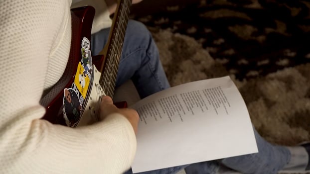 Musician playing electric guitar and looking at paper with printed song words lying on his knee. Man guitarist in creating song process. photo