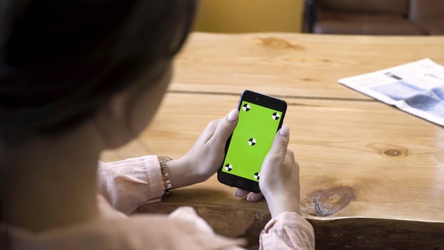 Close up of girl sitting at the table and using smartphone with green screen. Stock footage. View over the shoulder of a woman on the device with chromakey. photo