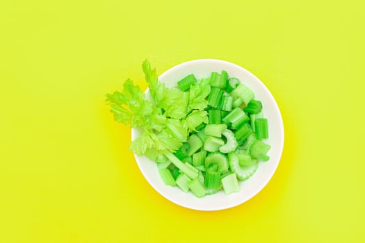 Fresh Chopped Celery Pieces with Water Drops in White Bowl on Yellow Background. Vegan and Vegetarian Culture. Raw Food. Healthy Diet with Negative Calorie Content photo