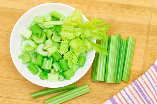 Fresh Chopped Celery Slices in White Bowl with Celery Sticks on Bamboo Cutting Board. Vegan and Vegetarian Culture. Raw Food. Healthy Diet with Negative Calorie Content photo