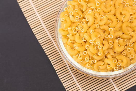 Uncooked Chifferi Rigati Pasta in Glass Jar on Bamboo Mat on Black Background. Fat and Unhealthy Food. Classic Dry Macaroni. Italian Culture and Cuisine. Raw Pasta photo