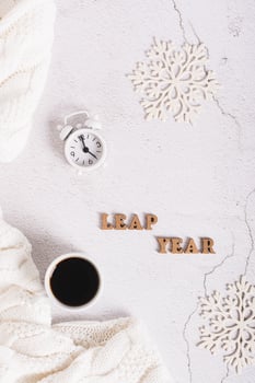 Leap year concept, coffee, alarm clock, snowflakes and letters on a light top and vertical view photo