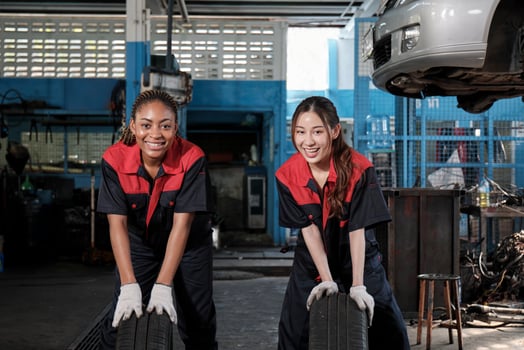 Two diverse female automotive mechanic worker partners compete to push car wheels for change and repair at garage, vehicle maintenance service jobs, industry occupation, and professional labor works. photo