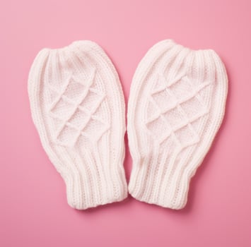 AI generated two knitted white mittens on a pink surface photo