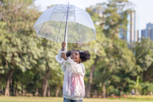 Cheerful child girl with an umbrella playing with rain in the park, Cute little kid girl playing outdoors in the garden photo