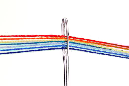 multi-colored threads for sewing in the form of a rainbow pass through an antique needle on a white background photo