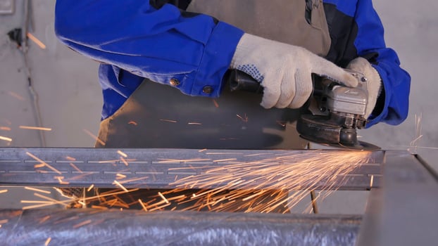 Craftsman sawing metal with disk grinder in workshop. Grinding metal with sparks flying. Electric wheel grinding on steel structure in factory Low speed shutter. Metal grinding with orange flying photo
