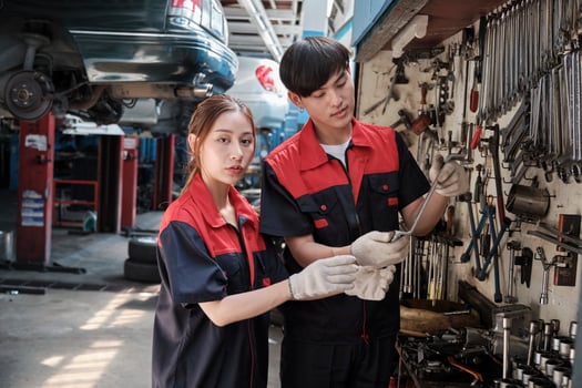 Two professional Asian mechanic partners discuss hand tools and machinery for fixing work at car service garage, maintenance jobs, and check and repair occupation in automotive industry business. photo
