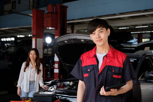 Portrait of young Asian male automotive mechanic worker with female customer's EV car at maintenance garage, happy smiles, professional service station, check and repair in auto transport industry. photo