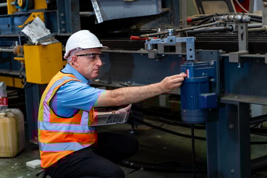 Caucasian industrial worker is using laptop computer to calibrating machine while inspecting inside the metal sheet galvanized roof factory for safety industry photo