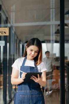 Young female hanging a welcome sign in front of a coffee shop. Beautiful waitress or hostess holding a tablet preparing  in a restaurant. photo