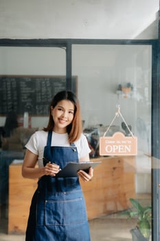 Young female hanging a welcome sign in front of a coffee shop. Beautiful waitress or hostess holding a tablet preparing  in a restaurant. photo