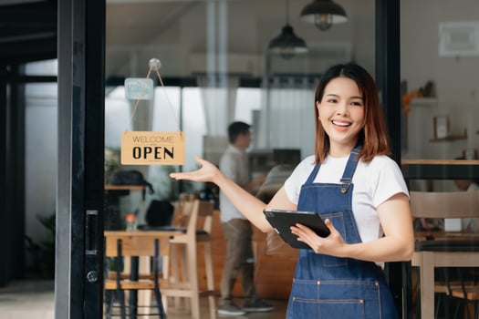 Young female hanging a welcome sign in front of a coffee shop. Beautiful waitress or hostess holding a tablet preparing  in a restaurant. photo