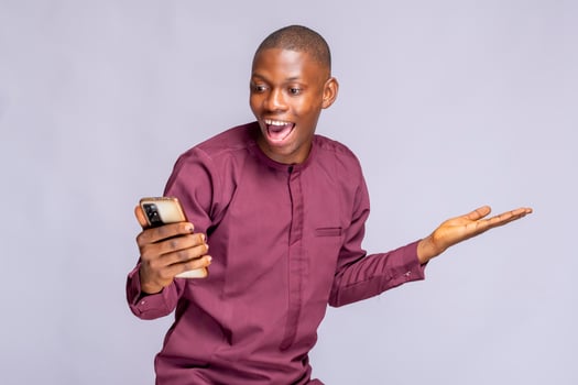 Super happy african guy in authentic costume using mobile phone celebrating success over white background, copy space photo