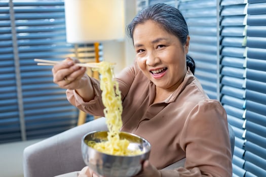 Senior Chinese woman using chopstick to eat noodle at home for cultural staple food and longevity concept photo