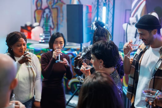 Diverse people crowd drinking alcohol beverages while celebrating in nightclub. Youn friends group holding glasses while socializing and partying on dancefloor at social gathering photo