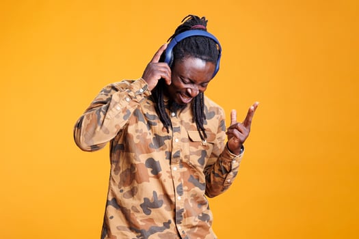 Cheerful young adult listening music using headset, dancing alone in studio over yellow background. Playful african american man enjoying joyful playlist, having fun on song rhythm photo
