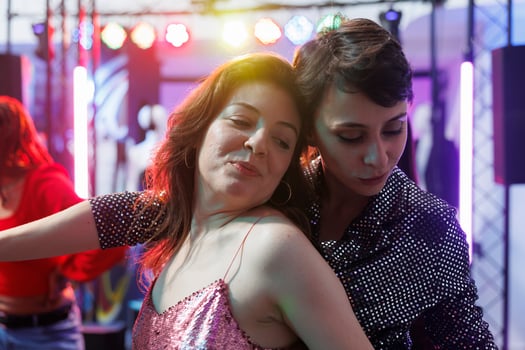 Smiling women hugging while dancing together at nightclub party. Young romantic girlfriends couple relaxing and moving on crowded dancefloor while clubbing at discotheque photo