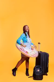 Tourist being excited about holiday trip, jumping in studio with inflatable and trolley bags. Female model preparing to travel abroad with suitcase, going on vacation journey. photo
