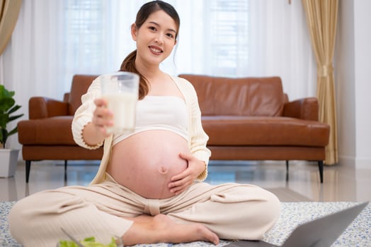 Pregnant woman drinking milk while sitting on the floor at home photo