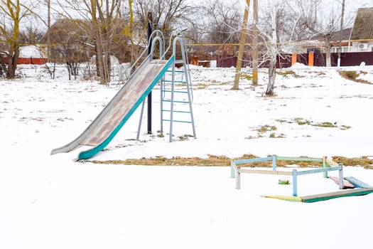 Children's playground in winter under snow. Swing, carousel and slide. Winter desolation photo