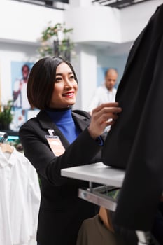 Clothing store smiling asian employee fastening jacket buttons while wearing mannequin in formal apparel. Shopping mall boutique woman worker organizing womenswear for sale photo