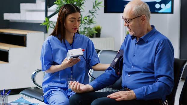 Assistant checking senior man cardiac pulse during cardiology examination in hospital waiting room. Asian nurse measuring patient blood pressure and hypertension using medical tonometer photo