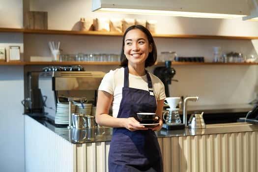 Portrait of asian smiling female barista, cafe waitress holding cup of coffee, serving clients, taking order to the tablet, standing near cafe counter photo