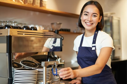Portrait of cute barista girl working behind counter, making coffee, steaming milk for cappuccino, wearing cafe uniform blue apron photo