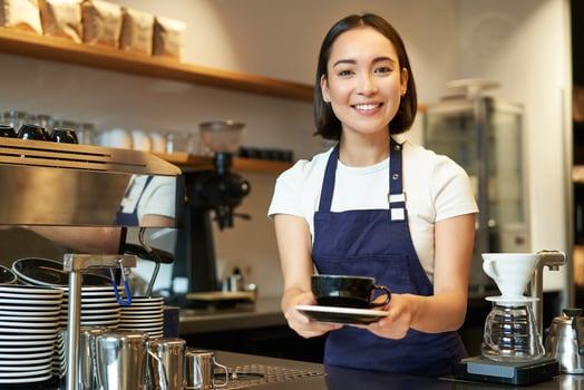 Portrait of smiling young woman providing customer service in cafe, holding cup of coffee, giving order to client, wearing apron uniform photo