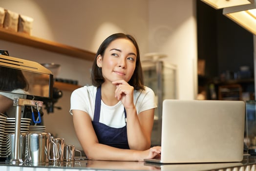 Portrait of girl barista with laptop, standing at counter in coffee shop and thinking, looking curious and thinking photo