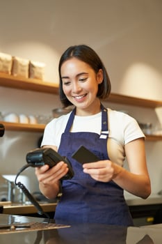 Portrait of smiling asian barista, coffee shop employee using POS terminal and credit card, helps client pay contactless in cafe photo