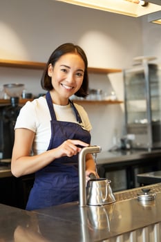 Vertical shot of barista, girl in coffee shop, pouring water in kettle, preparing order in cafe, smiling at camera photo