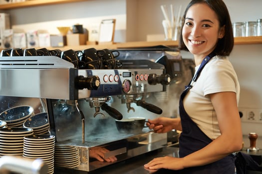 Smiling cute korean girl, barista working with coffee machine, prepare cappuccino, using steamr at cafe counter photo