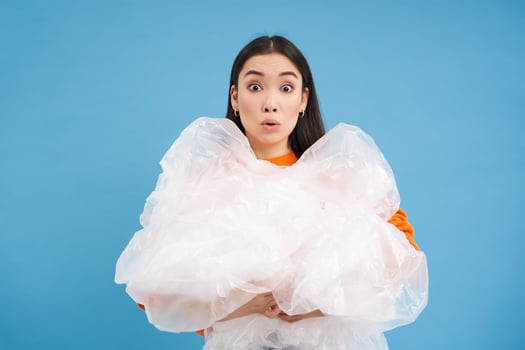Asian female eco-activist, woman looks surprised, holds plastic waste, preserving nature, standing over blue background photo