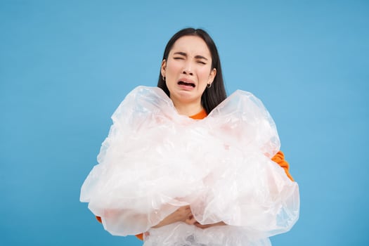 Annoyed woman holding loads of plastic in hands, looking bothered with sorting trash, eco-activist fighting for nature preservation, blue background photo