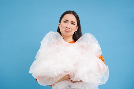Annoyed woman holding loads of plastic in hands, looking bothered with sorting trash, eco-activist fighting for nature preservation, blue background photo
