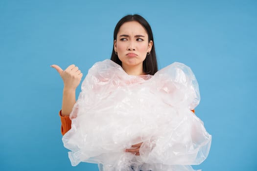 Unhappy korean woman with plastic waste, collecting garbage and pointing left with sad face, blue background photo