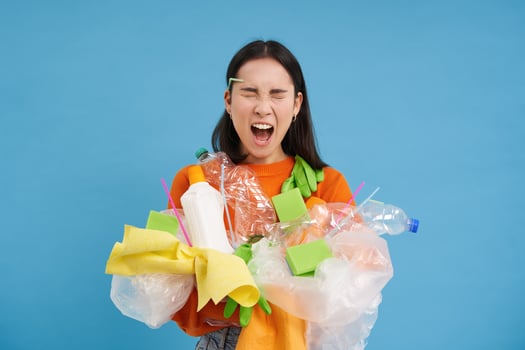 Shocked eco activist, collects loads of plastic to recycle, looking upset at bottles and unsorted garbage, blue background photo