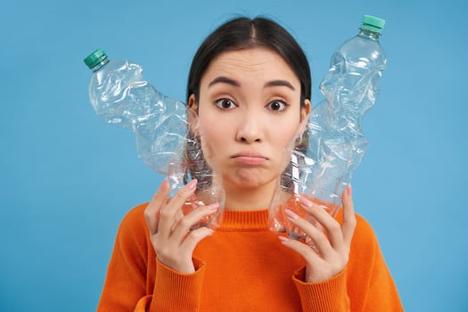 Portrait of sad asian woman with plastic bottles, upset by lack of recycling centers, blue background photo