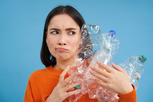 Annoyed korean woman looking with blaming face, holding plastic bottles, standing over blue studio background photo