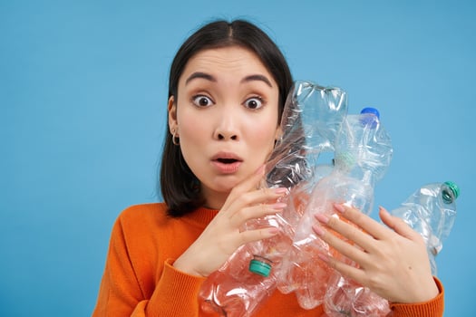 Surprised korean woman, holding plastic bottles, looking shocked at camera, concept of environment and recycling, blue background photo