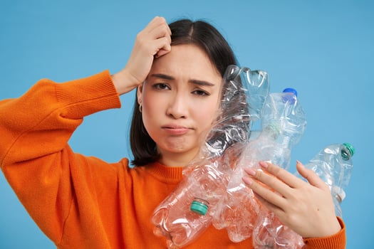 Troubled asian woman holding plastic bottles, trying find recycling center, blue background photo