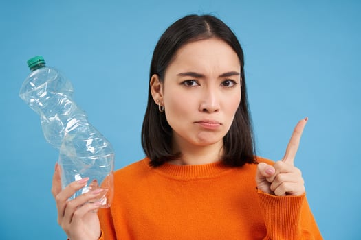 Serious asian woman tells to recycle, shows plastic bottle and urges sort and collect waste to recycling centers, blue background photo