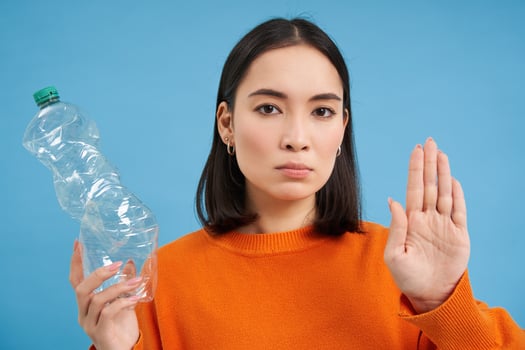 Serious asian woman tells to recycle, shows plastic bottle and urges sort and collect waste to recycling centers, blue background photo