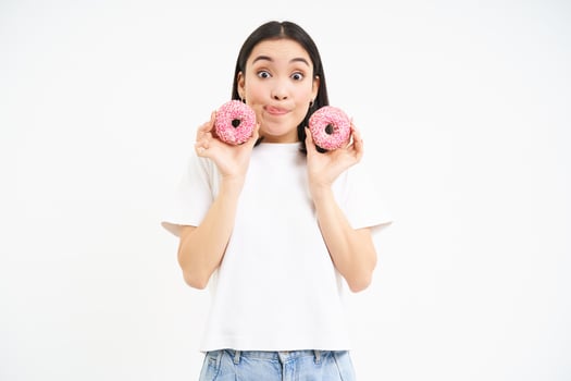 Cute young woman with two tasty doughnuts, tempted to try glazed donnuts, white background photo