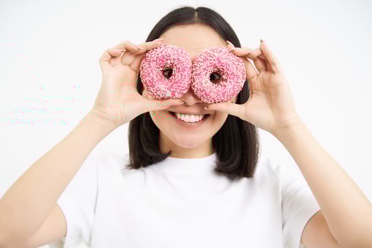 Image of funny young woman, makes glasses with two pink glazed doughnuts, looking through donnut holes and smiling, isolated on white background photo