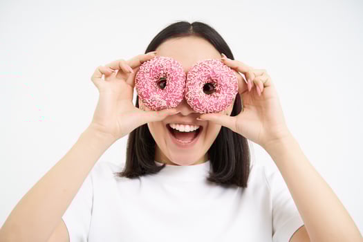 Funny smiling korean woman, holding two glazed pink doughnuts, eating dessert with happy face, white background photo