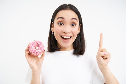 Image of girl having an idea, eureka moment, holding pink glazed doughnut and pointing up, white background photo