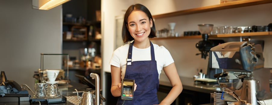 Portrait of asian barista girl at counter, showing card machine to client who wants to pay contactless, taking order, standing in cafe photo
